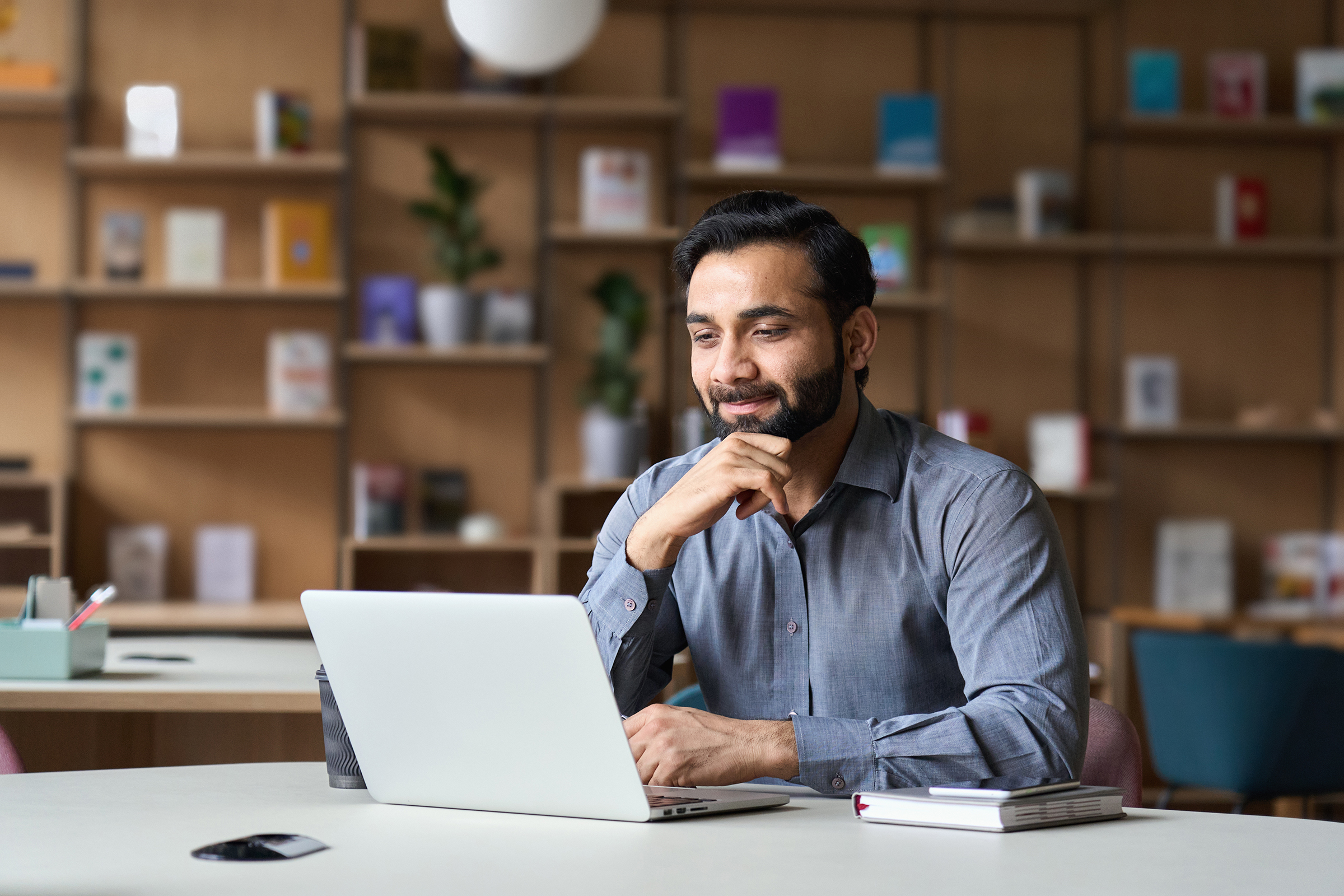 Bearded indian business man watching online webinar on laptop computer.